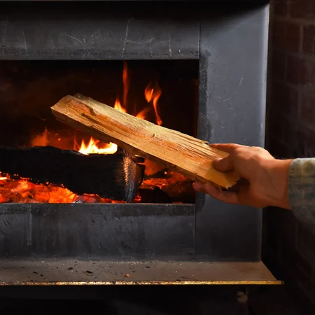 A fireplace with man placing a new log inside